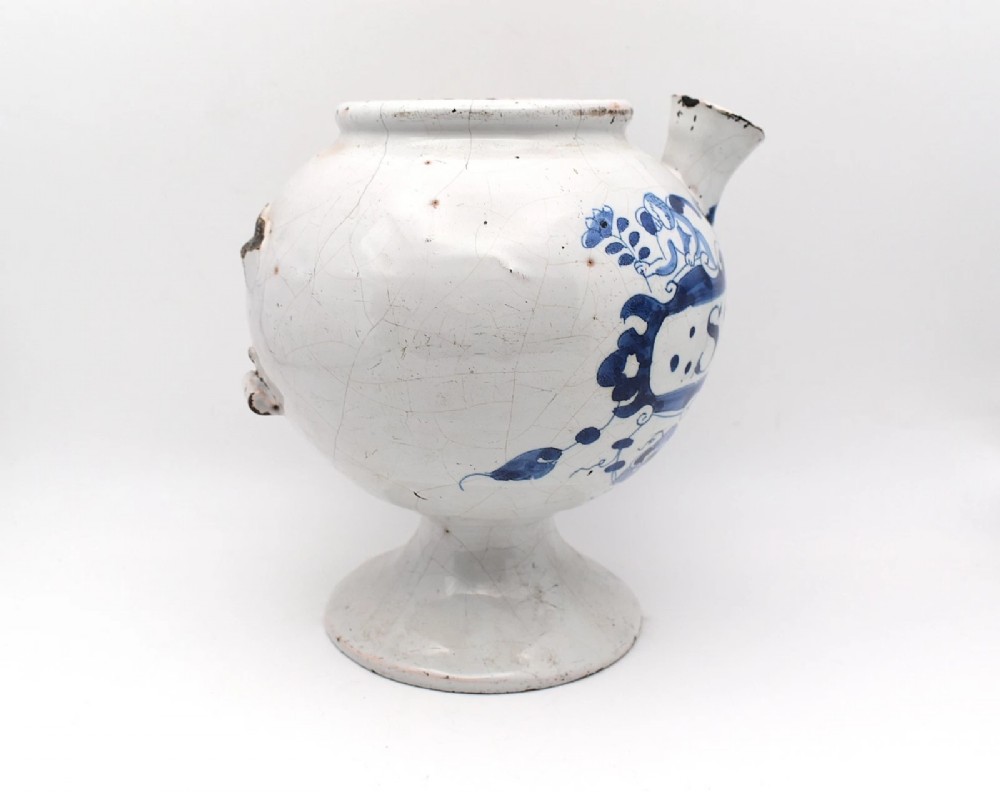 An 18th-century English delftware apothecary wet drug jar decorated in cobalt blue and white with a pouring spout, footed base, cherub motif, and the inscription S: BALSAM. View II