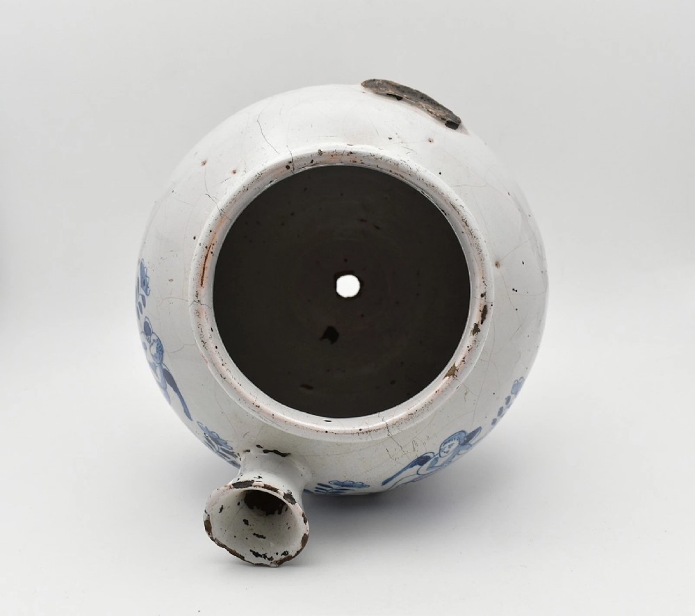 An 18th-century English delftware apothecary wet drug jar decorated in cobalt blue and white with a pouring spout, footed base, cherub motif, and the inscription S: BALSAM. View VII