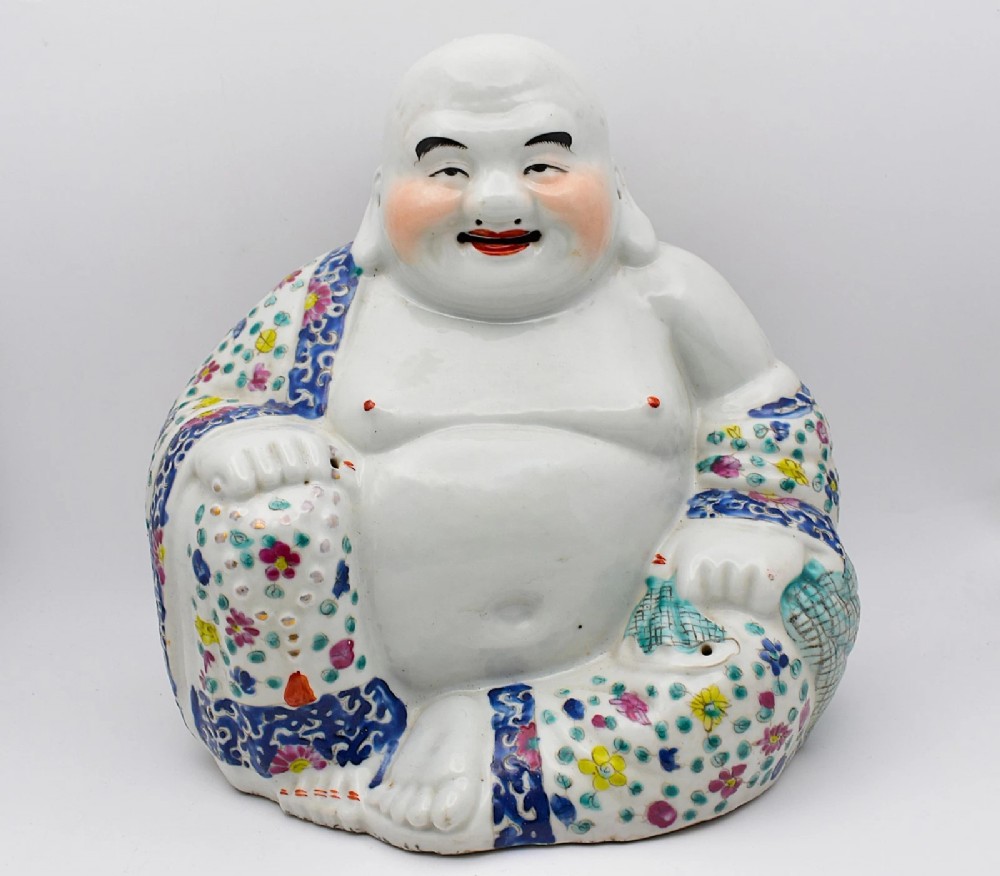 A seated twentieth-century Chinese famille rose porcelain figure of a laughing Budai draped in a floral enamelled robe.
