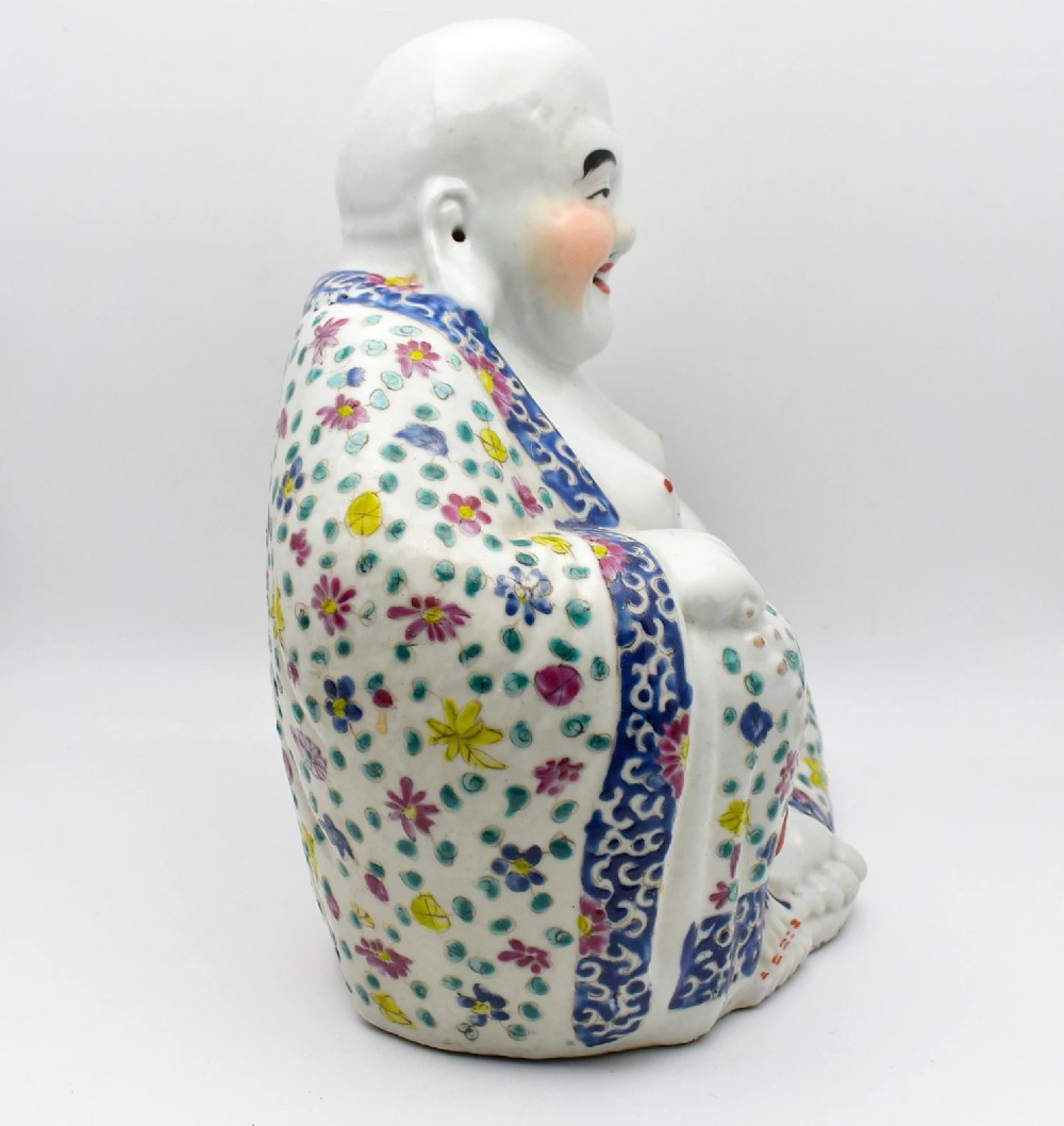 A seated twentieth-century Chinese famille rose porcelain figure of a laughing Budai draped in a floral enamelled robe. View IV