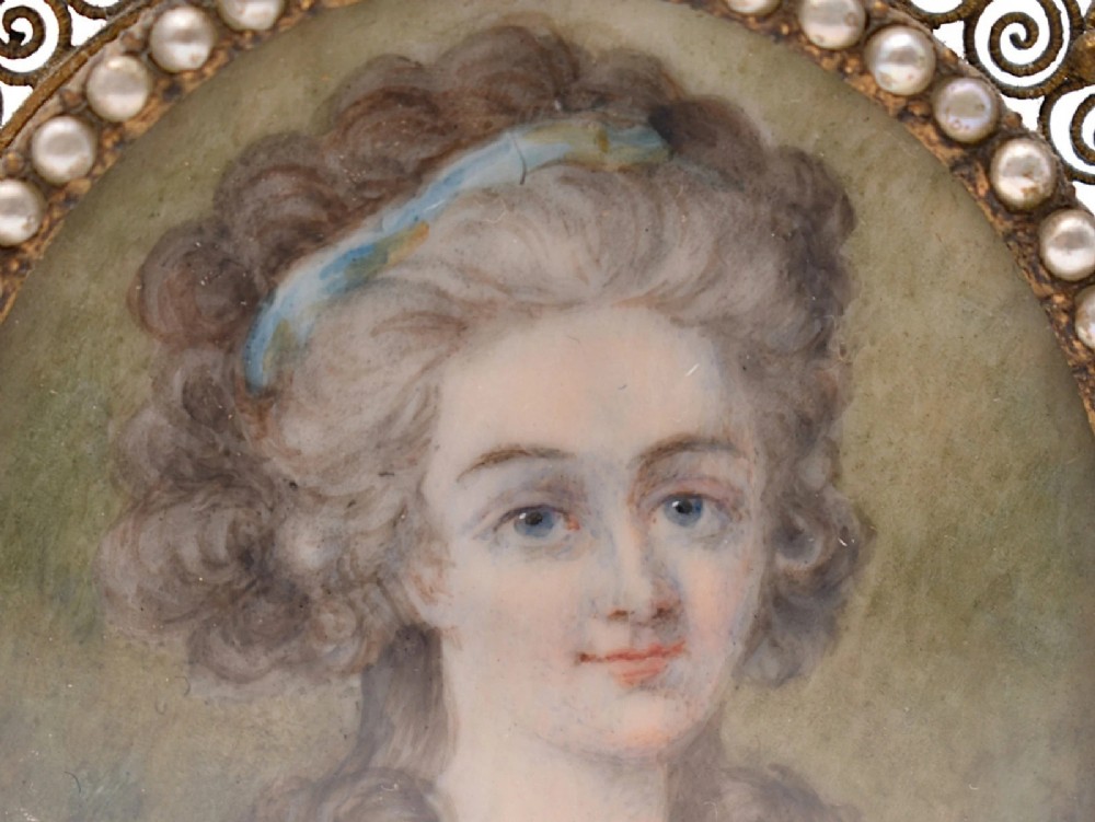 An 18th-century oval watercolour portrait miniature depicting a woman with curled hair, housed within a seed pearl bezel and a gilt filigree rectangular frame. View IV