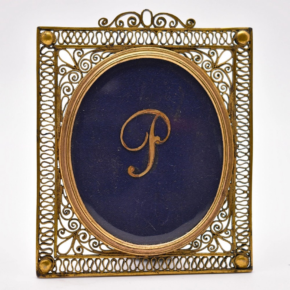 An 18th-century oval watercolour portrait miniature depicting a woman with curled hair, housed within a seed pearl bezel and a gilt filigree rectangular frame. View V