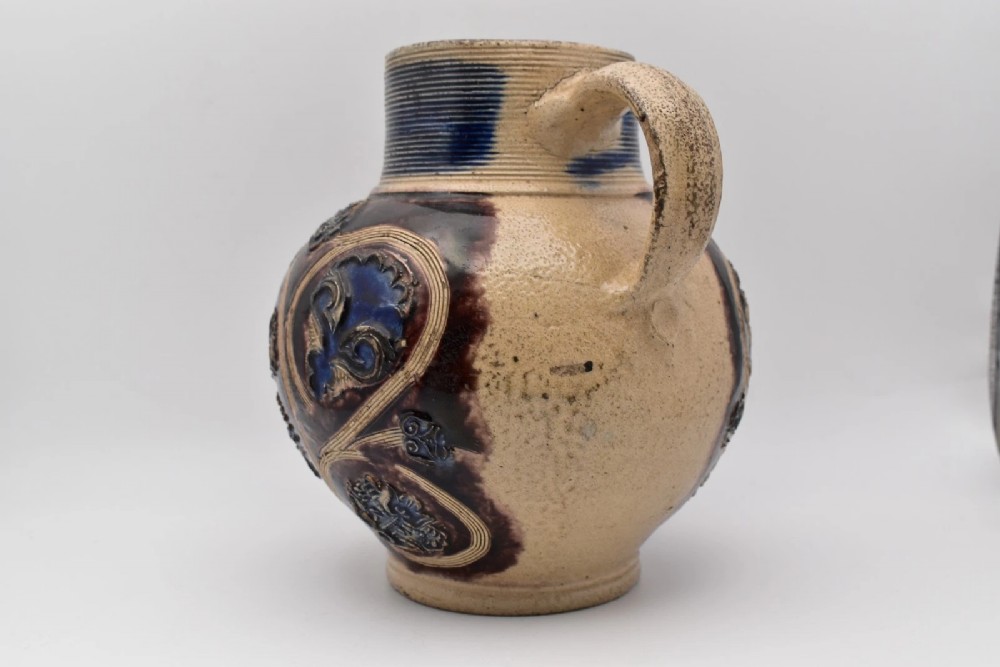 A seventeenth-century salt-glazed Westerwald stoneware jug decorated with cobalt blue and manganese violet glazes, featuring a central medallion with a royal portrait profile. View IV