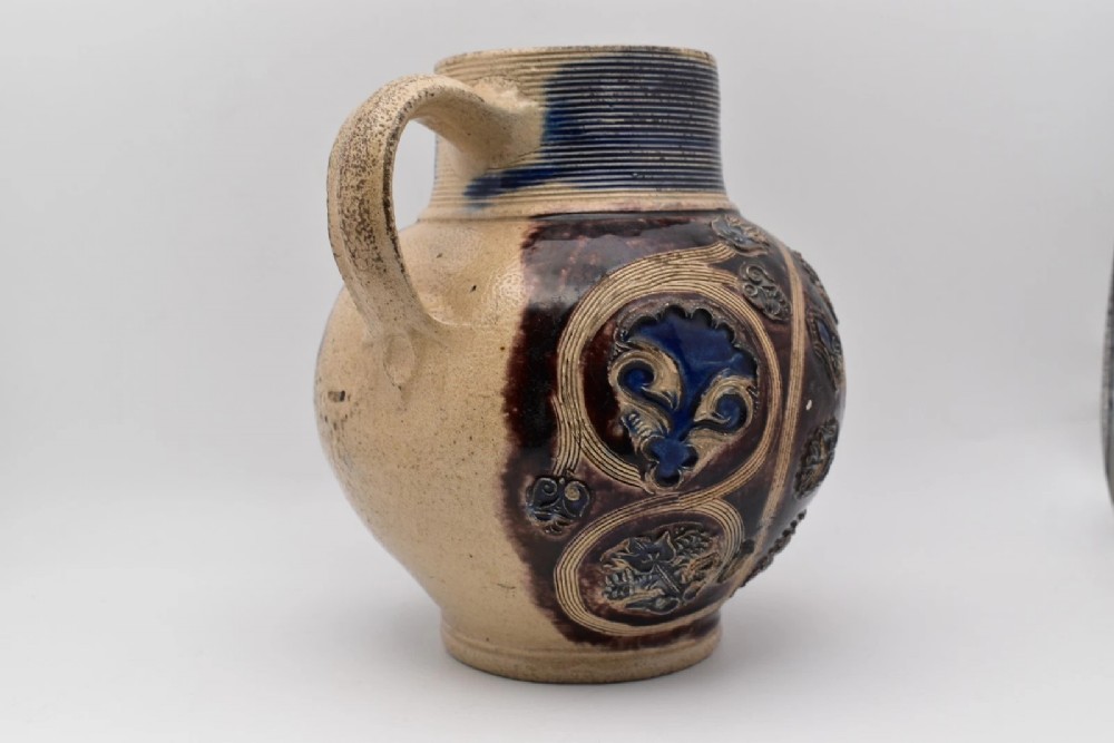 A seventeenth-century salt-glazed Westerwald stoneware jug decorated with cobalt blue and manganese violet glazes, featuring a central medallion with a royal portrait profile. View V
