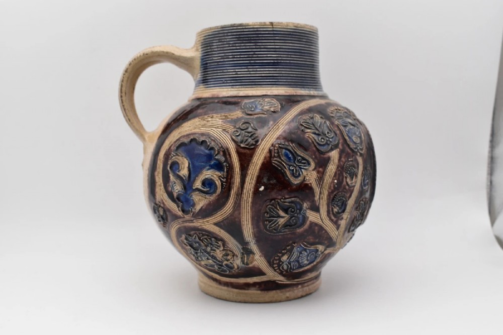 A seventeenth-century salt-glazed Westerwald stoneware jug decorated with cobalt blue and manganese violet glazes, featuring a central medallion with a royal portrait profile. View VI