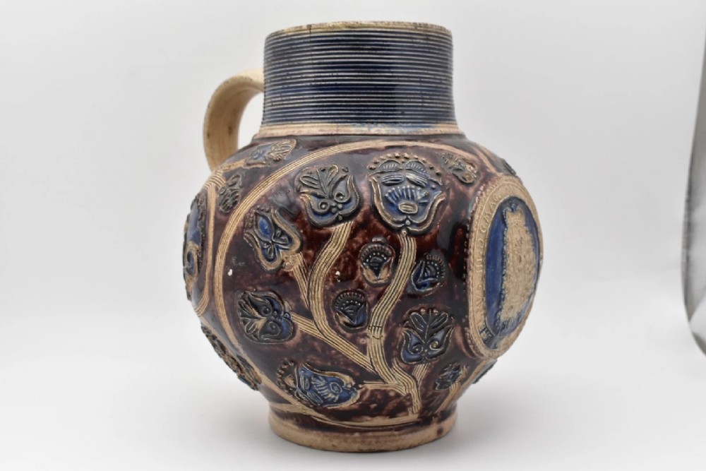 A seventeenth-century salt-glazed Westerwald stoneware jug decorated with cobalt blue and manganese violet glazes, featuring a central medallion with a royal portrait profile. View VII