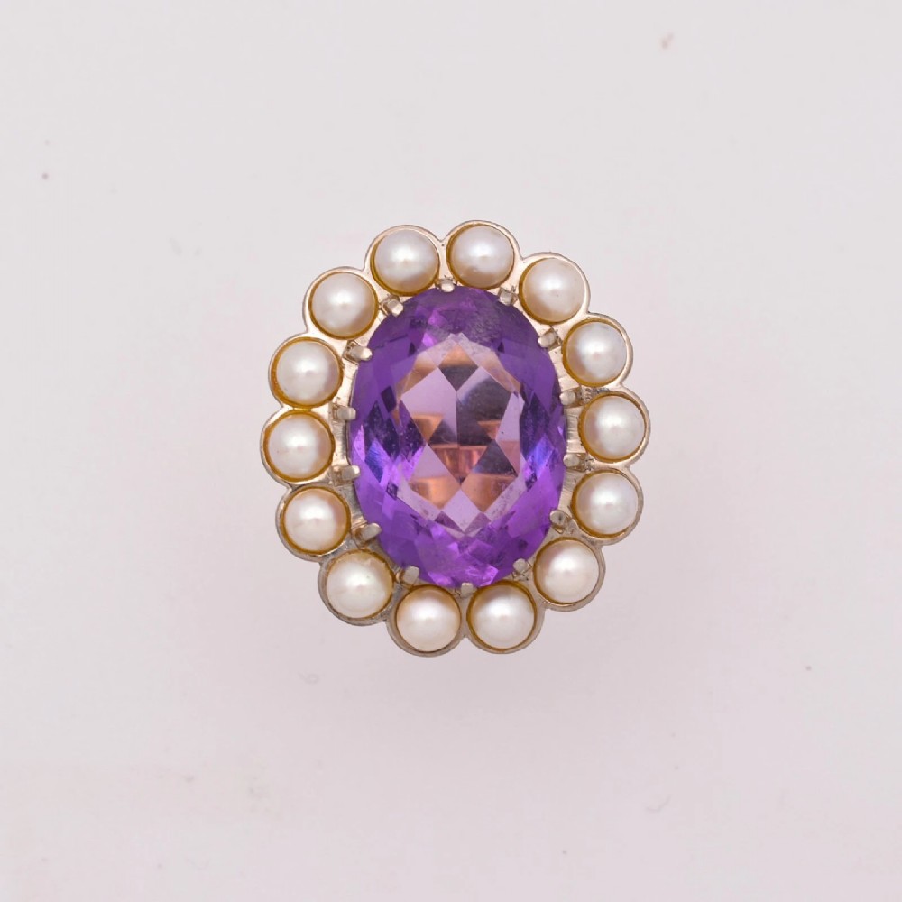 An 18ct yellow gold cluster ring featuring a centrally set oval faceted purple amethyst surrounded by a halo of fourteen small white pearls.
