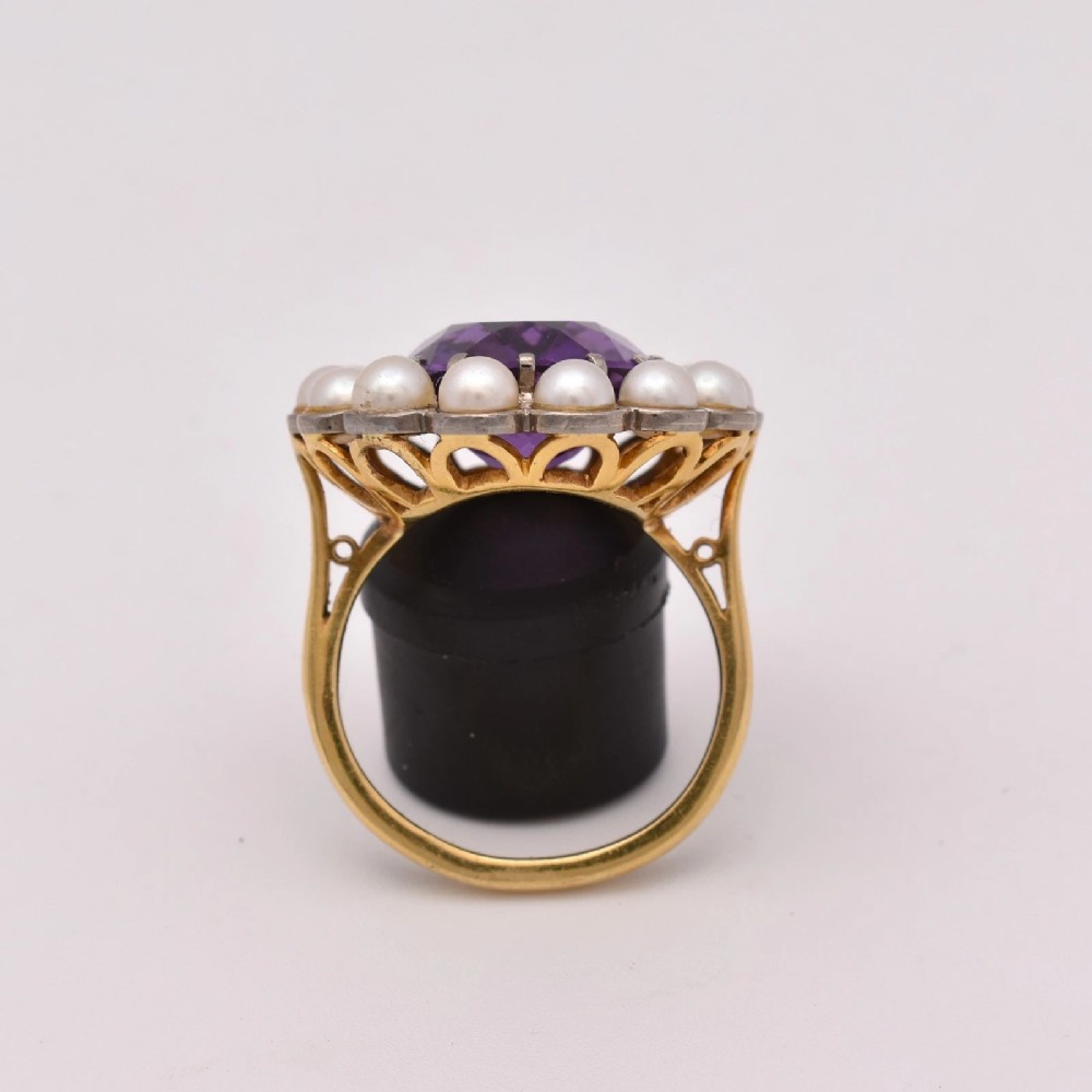 An 18ct yellow gold cluster ring featuring a centrally set oval faceted purple amethyst surrounded by a halo of fourteen small white pearls. View II