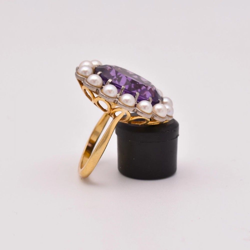 An 18ct yellow gold cluster ring featuring a centrally set oval faceted purple amethyst surrounded by a halo of fourteen small white pearls. View III