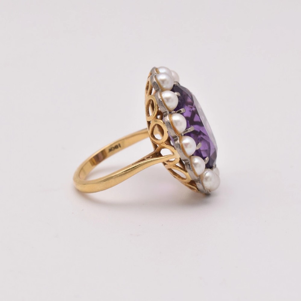 An 18ct yellow gold cluster ring featuring a centrally set oval faceted purple amethyst surrounded by a halo of fourteen small white pearls. View IV