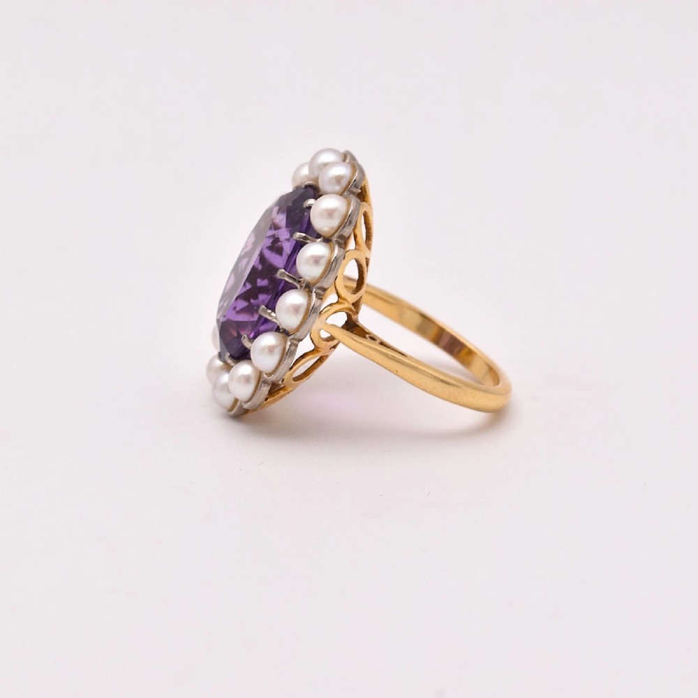 An 18ct yellow gold cluster ring featuring a centrally set oval faceted purple amethyst surrounded by a halo of fourteen small white pearls. View V