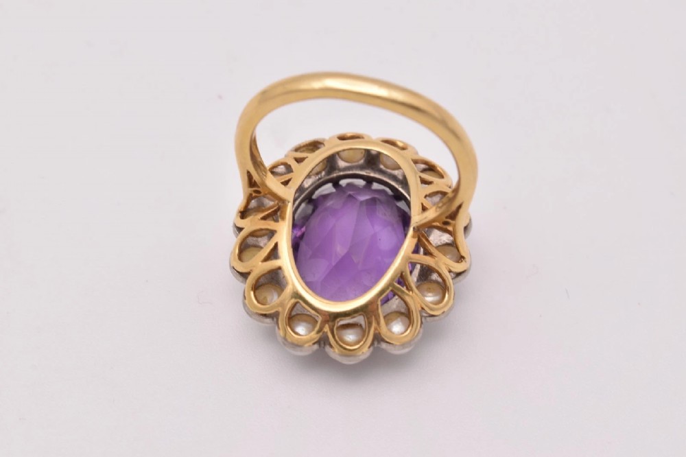 An 18ct yellow gold cluster ring featuring a centrally set oval faceted purple amethyst surrounded by a halo of fourteen small white pearls. View VII