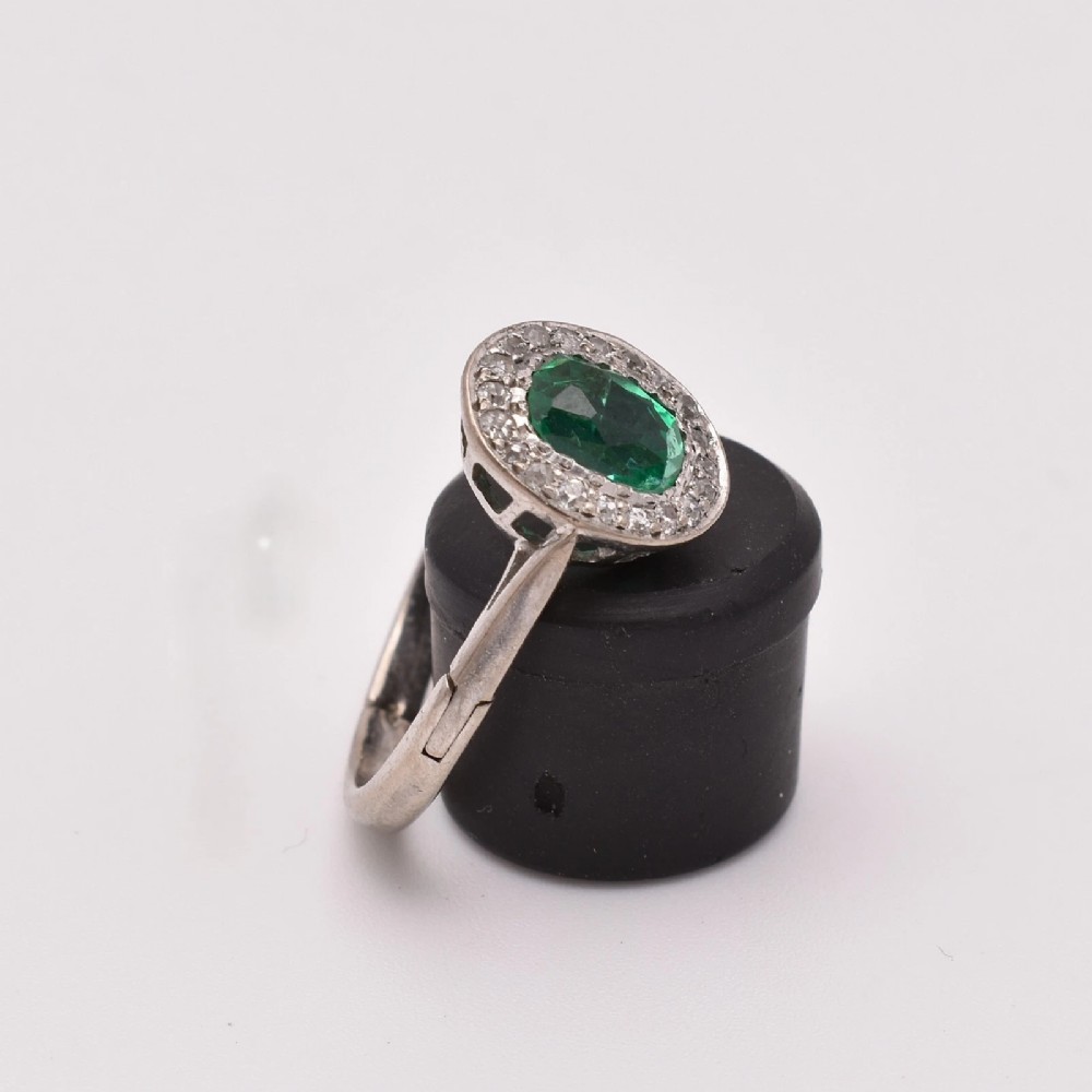 An oval green emerald set at the centre of a white gold cluster ring surrounded by small diamonds with an adjustable band. View III