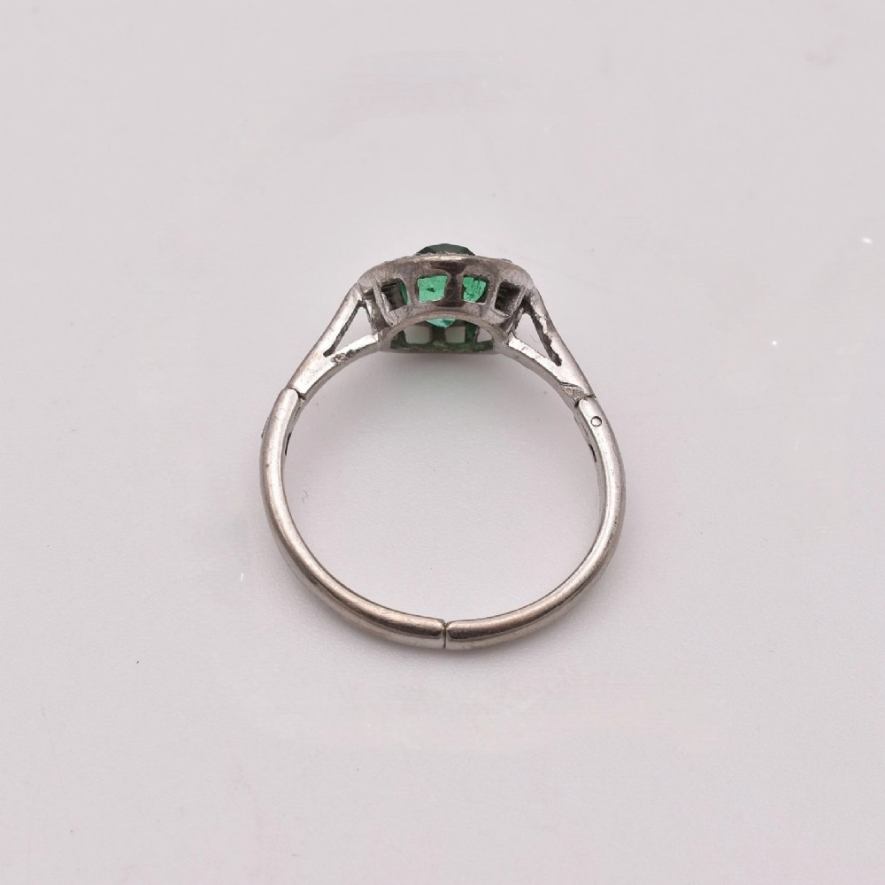 An oval green emerald set at the centre of a white gold cluster ring surrounded by small diamonds with an adjustable band. View VIII