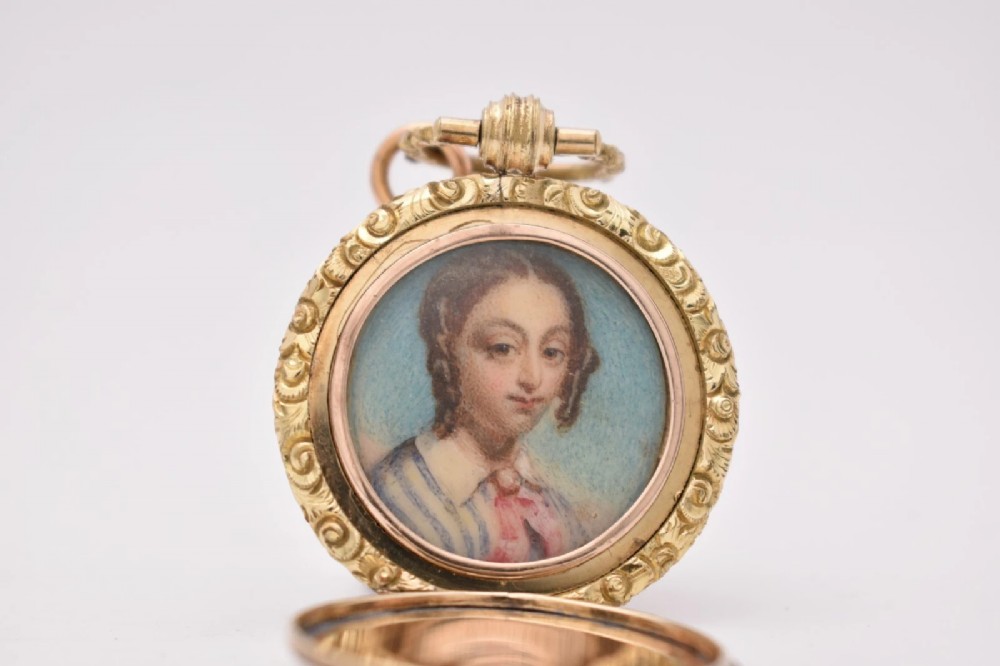 A circular gold locket pendant featuring a hand-painted portrait of a woman with dark hair against a light blue background. View II