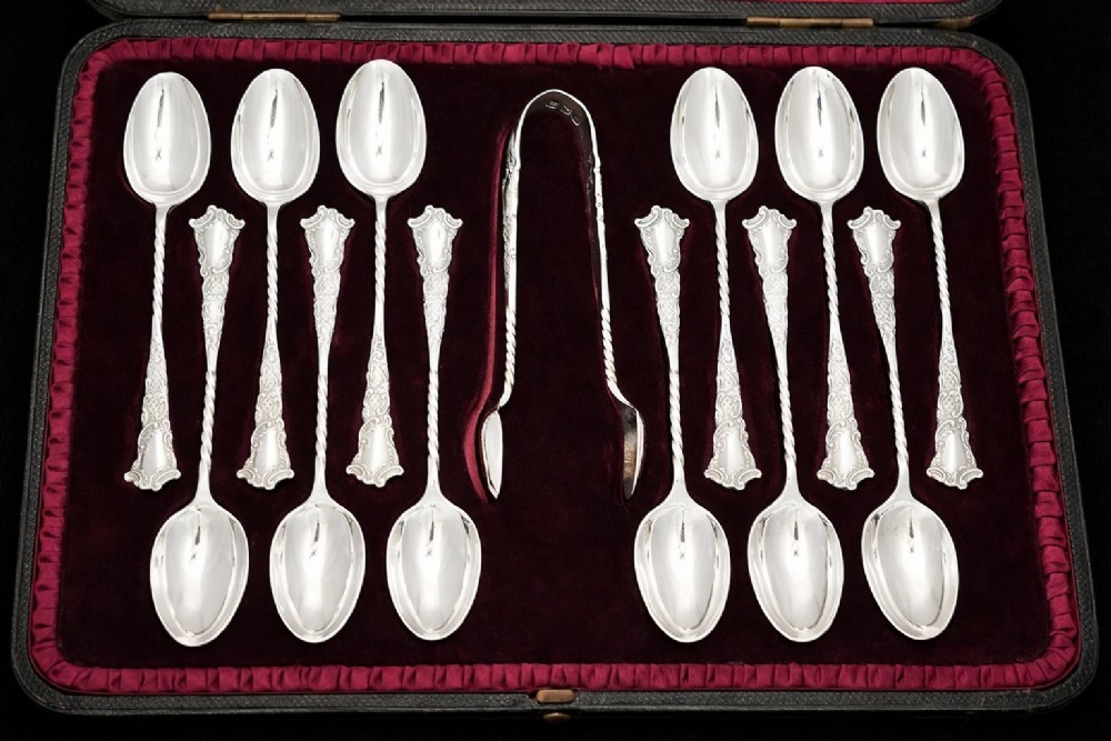 A set of twelve silver teaspoons with twisted stems and matching sugar tongs arranged inside a fitted burgundy velvet-lined case. View II