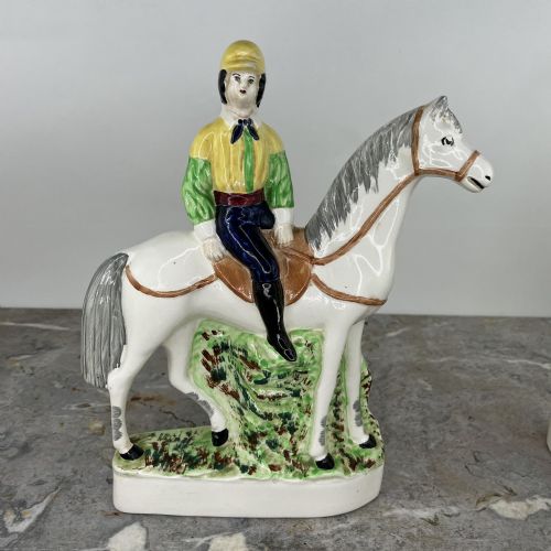 fig 1. A pair of hand-painted earthenware Staffordshire flatback figures depicting jockeys wearing yellow and green silks mounted on white horses.