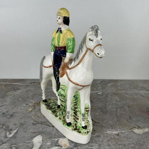fig 2. A pair of hand-painted earthenware Staffordshire flatback figures depicting jockeys wearing yellow and green silks mounted on white horses.
