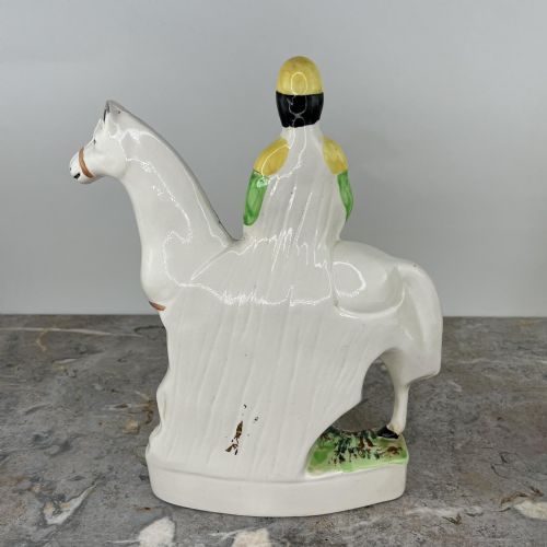 fig 3. A pair of hand-painted earthenware Staffordshire flatback figures depicting jockeys wearing yellow and green silks mounted on white horses.
