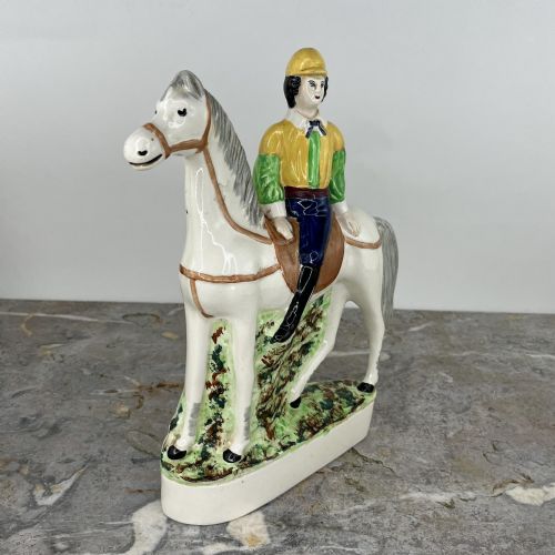 fig 5. A pair of hand-painted earthenware Staffordshire flatback figures depicting jockeys wearing yellow and green silks mounted on white horses.