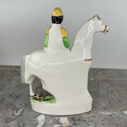 fig 6. A pair of hand-painted earthenware Staffordshire flatback figures depicting jockeys wearing yellow and green silks mounted on white horses.
