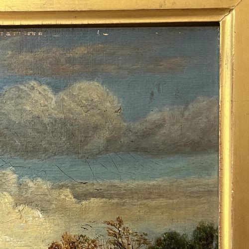fig 6. A 19th-century oil painting featuring a figure walking along a dirt pathway towards a distant church spire under a sky filled with clouds, set within a wide gold frame.
