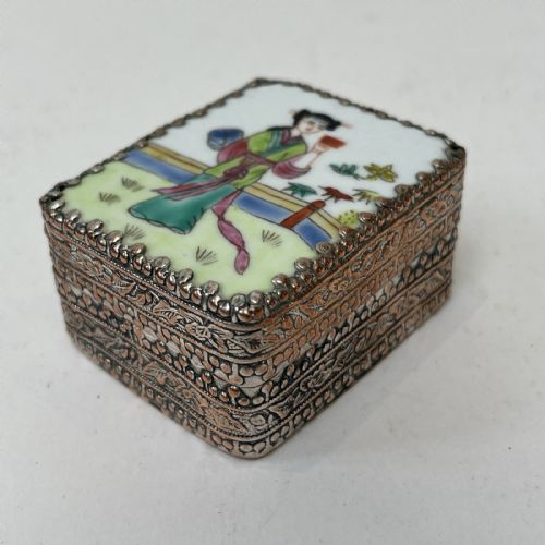 fig 8. A small rectangular silver-plated metal pill box with intricately chased foliate sides and a hand-painted enamel lid depicting a figure in green traditional dress.