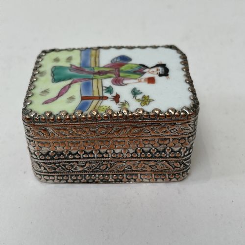 fig 9. A small rectangular silver-plated metal pill box with intricately chased foliate sides and a hand-painted enamel lid depicting a figure in green traditional dress.