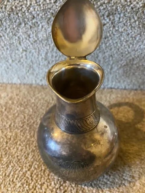 fig 1. A small bulbous silver-plated pitcher featuring a hinged lid, thumbpiece, curved handle, and a ribbed decorative collar.