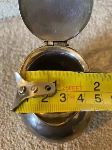 fig 7. A small bulbous silver-plated pitcher featuring a hinged lid, thumbpiece, curved handle, and a ribbed decorative collar.