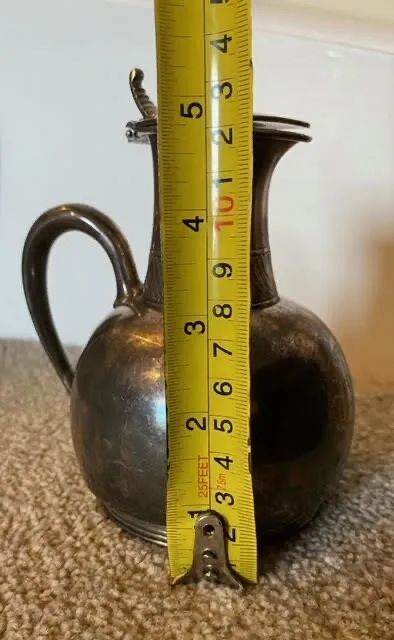 fig 8. A small bulbous silver-plated pitcher featuring a hinged lid, thumbpiece, curved handle, and a ribbed decorative collar.