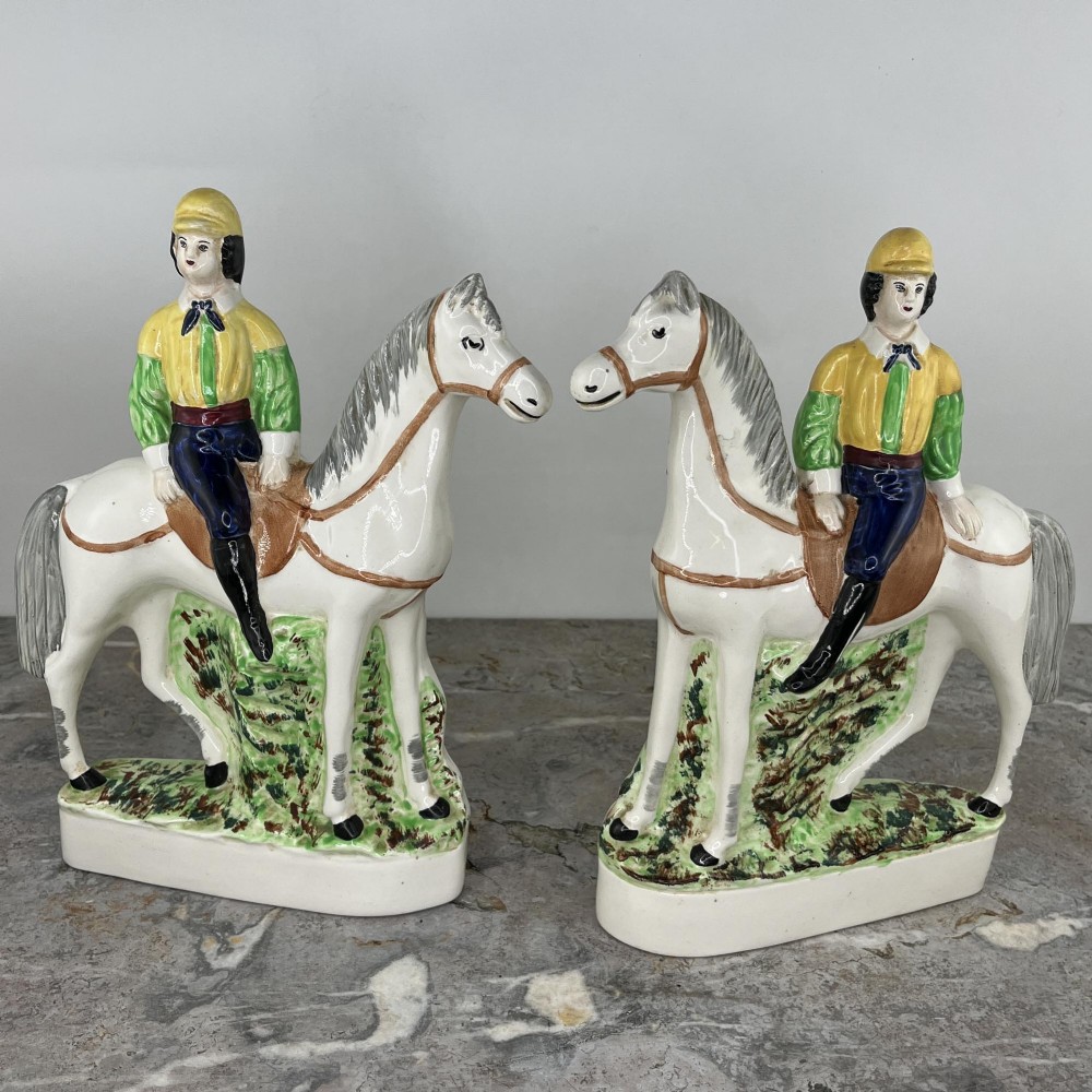 A pair of hand-painted earthenware Staffordshire flatback figures depicting jockeys wearing yellow and green silks mounted on white horses.
