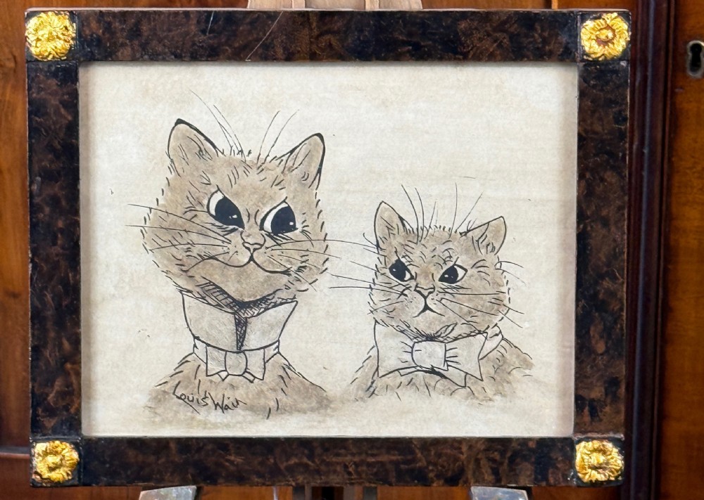 An original pen and ink drawing of two anthropomorphic cats wearing collars, set within a dark patterned wooden frame with gilt corner rosettes.