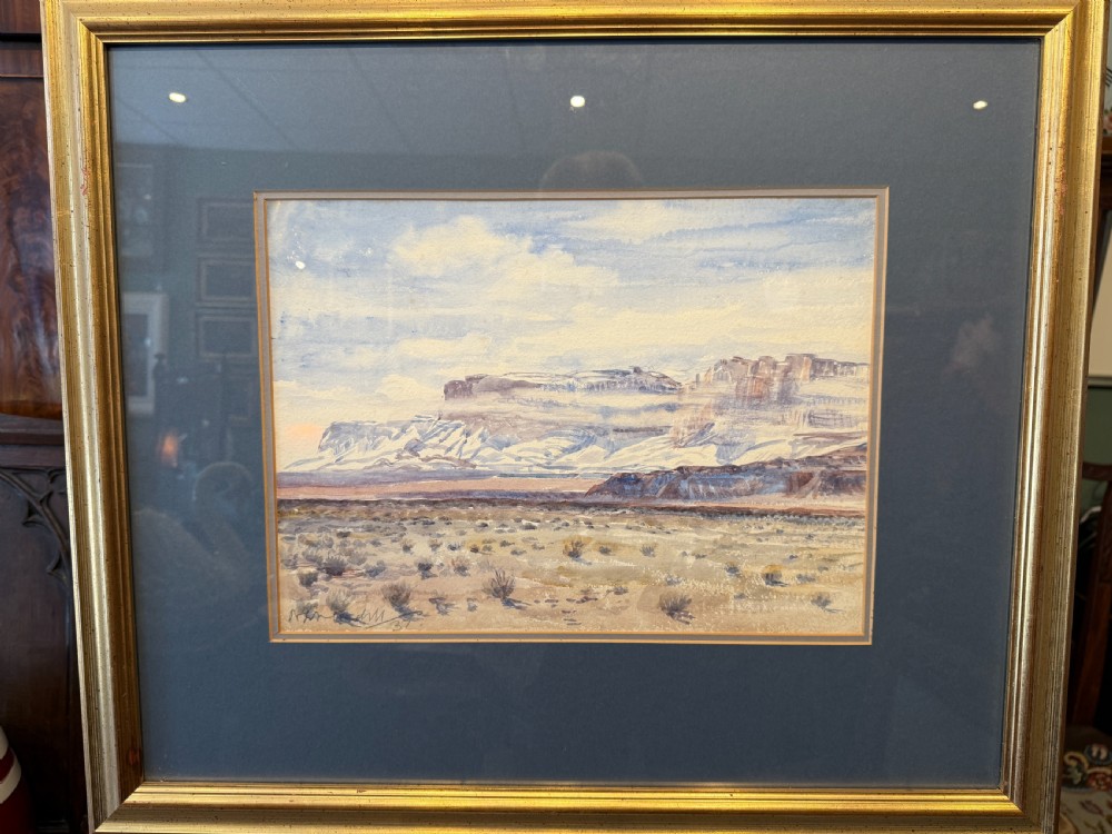 A framed watercolour painting depicting an expansive desert plain leading towards distant rock formations under a light blue sky.