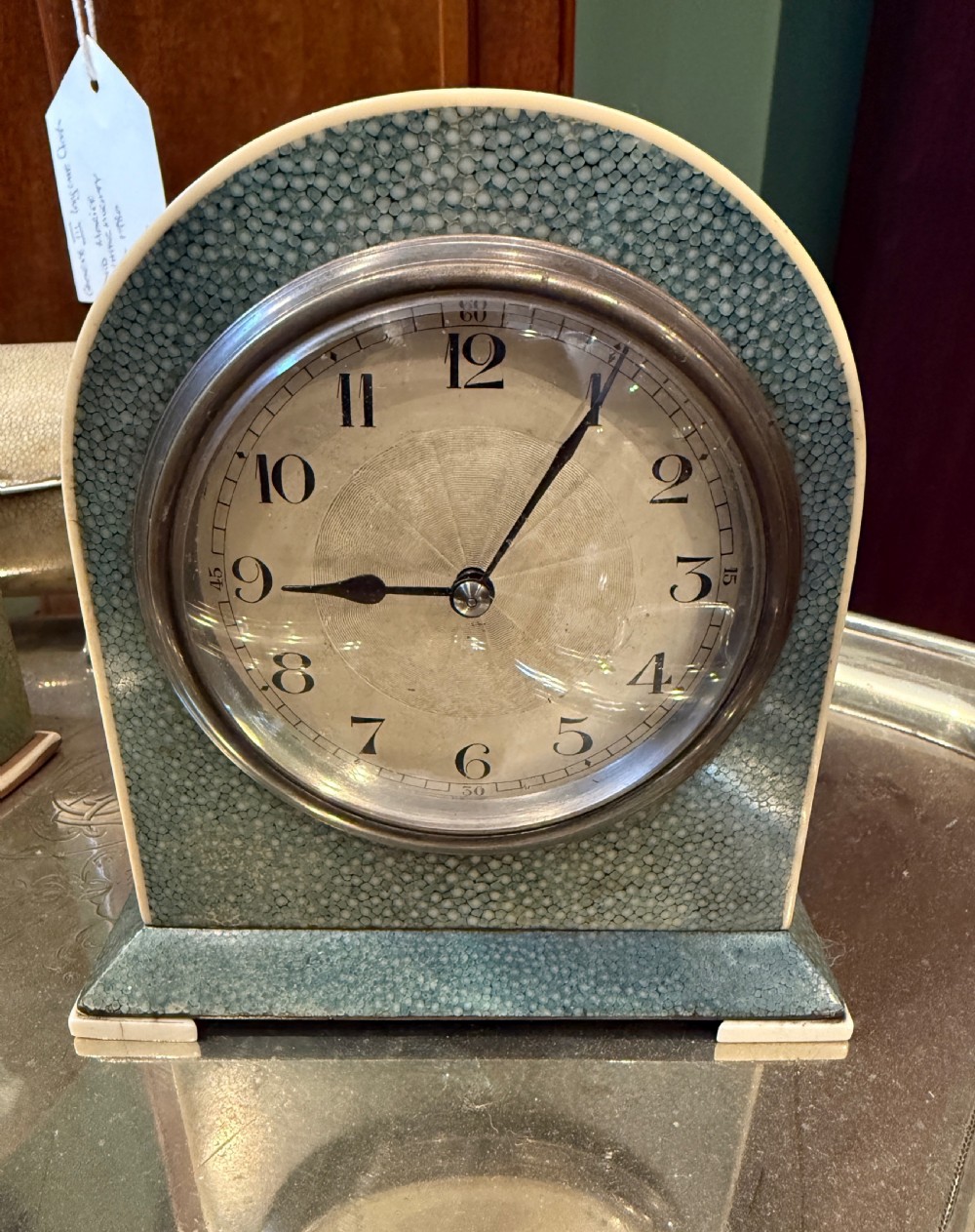 An Art Deco arched table clock clad in green shagreen with ivorine trim, a silvered dial, and black Arabic numerals.