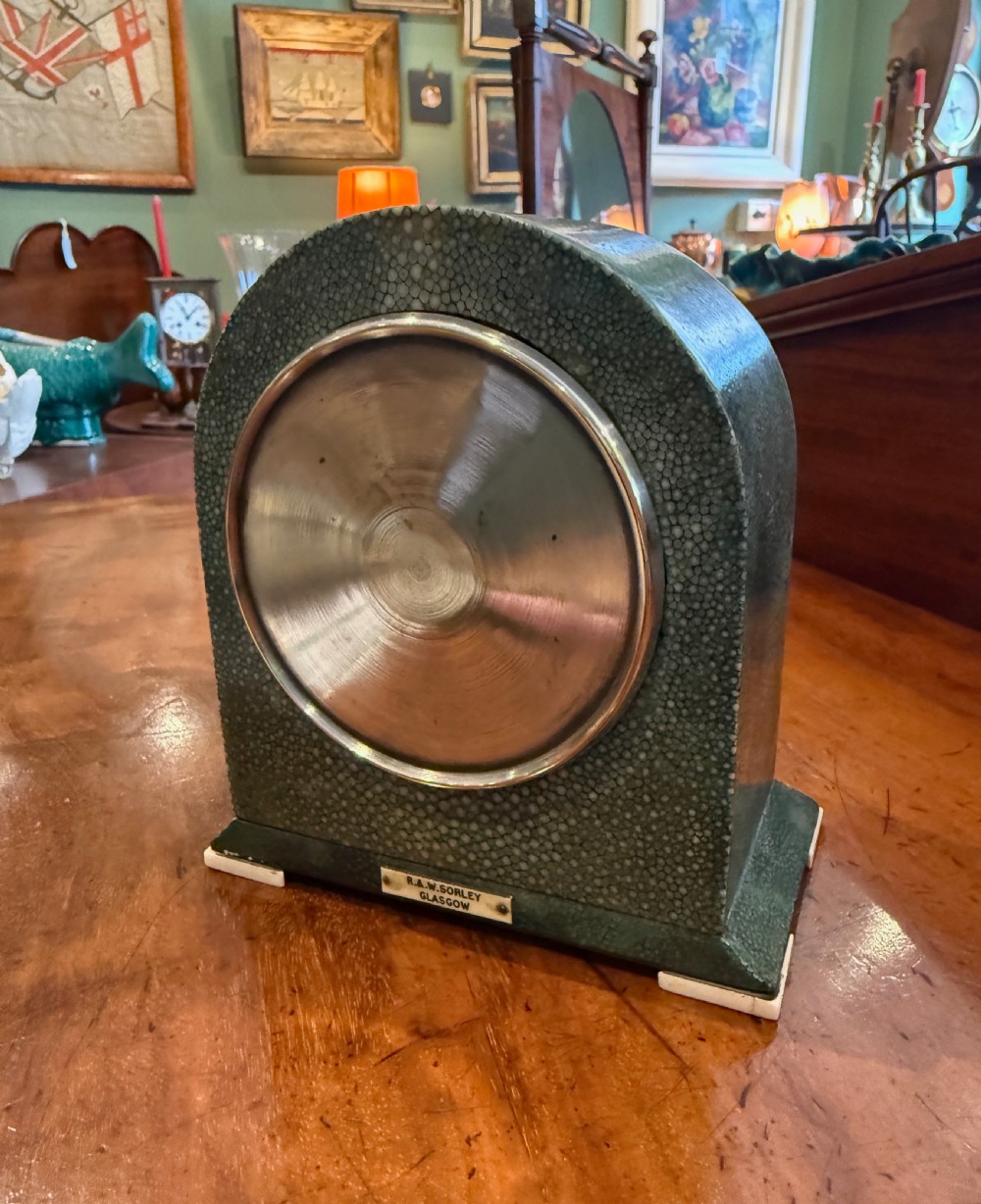 An Art Deco arched table clock clad in green shagreen with ivorine trim, a silvered dial, and black Arabic numerals. View V