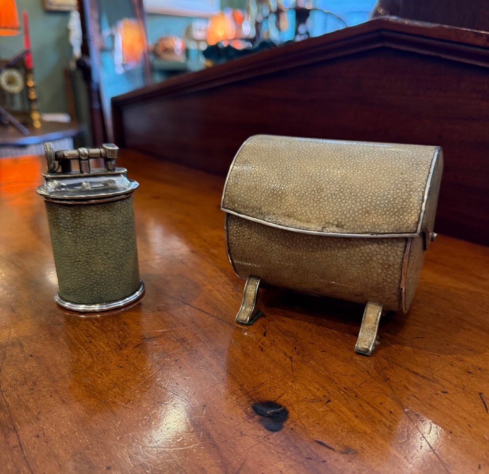 An Art Deco smoking set comprising a sage green shagreen cylindrical table lighter with silver metal fittings alongside a cream shagreen domed cigarette box resting on four small silver feet.