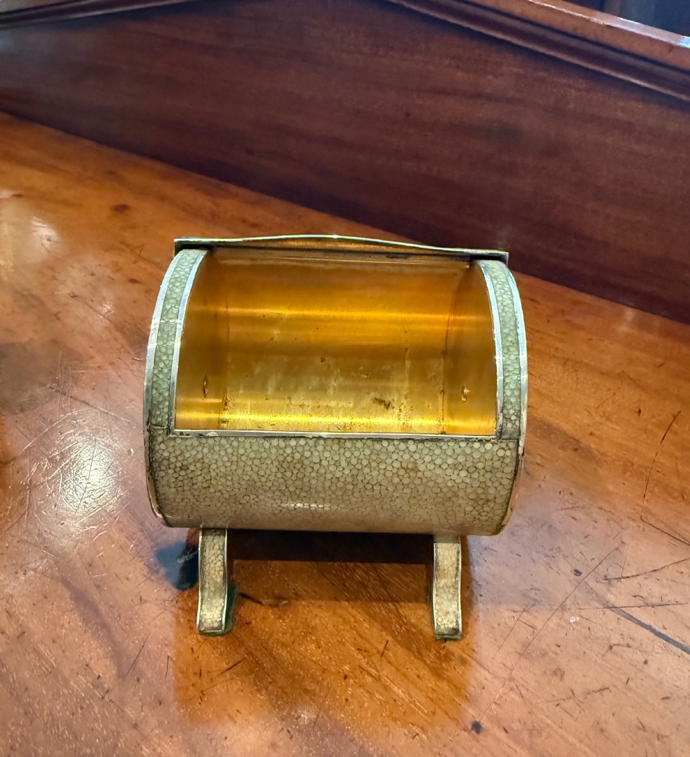 An Art Deco smoking set comprising a sage green shagreen cylindrical table lighter with silver metal fittings alongside a cream shagreen domed cigarette box resting on four small silver feet. View II