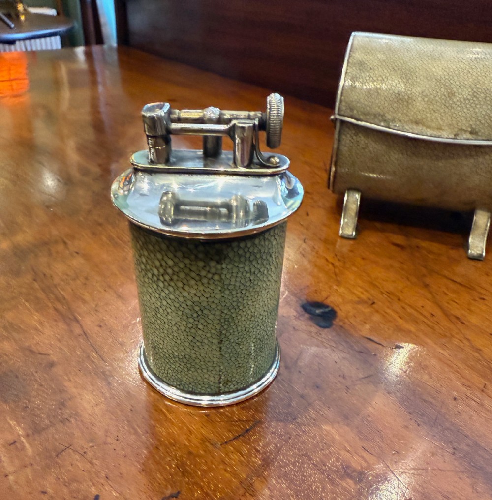 An Art Deco smoking set comprising a sage green shagreen cylindrical table lighter with silver metal fittings alongside a cream shagreen domed cigarette box resting on four small silver feet. View IV