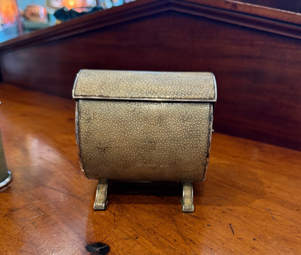 An Art Deco smoking set comprising a sage green shagreen cylindrical table lighter with silver metal fittings alongside a cream shagreen domed cigarette box resting on four small silver feet. View VII