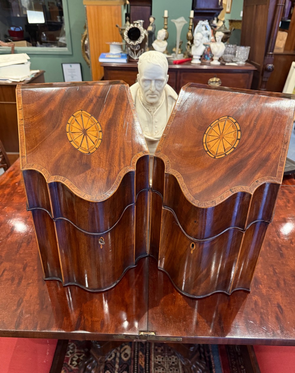 A pair of Georgian flame mahogany knife boxes featuring sloped lids, serpentine fronts, and oval patera marquetry inlays.