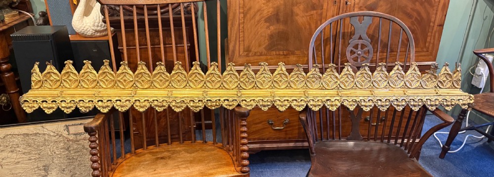 A pair of long Victorian gilt brass curtain pelmets featuring ornate Gothic cresting and pierced geometric star tracery.
