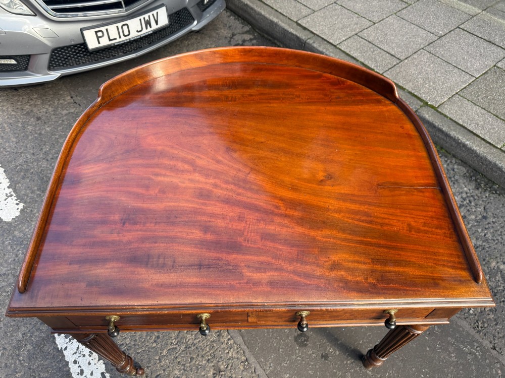 A Mid-Victorian mahogany writing desk featuring a low three-sided gallery top, two frieze drawers with brass drop handles, and reeded tapered legs on castors. View III