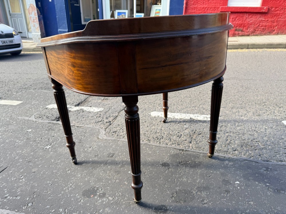 A Mid-Victorian mahogany writing desk featuring a low three-sided gallery top, two frieze drawers with brass drop handles, and reeded tapered legs on castors. View IV