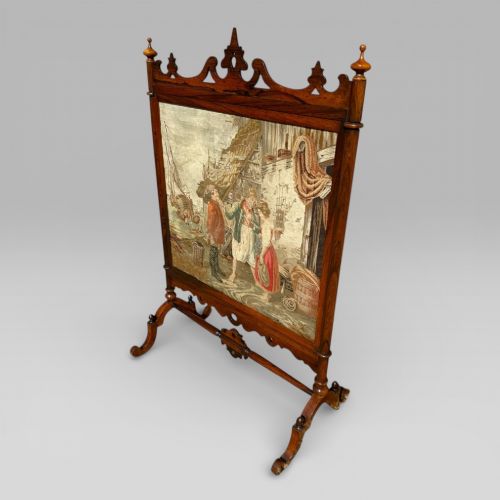 fig 1. A Victorian rosewood cheval fire screen featuring a carved wooden frame with finials and an embroidered textile panel depicting figures near a coastal cottage.