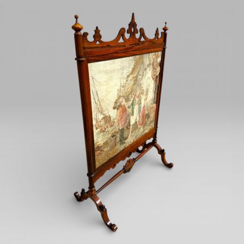 fig 2. A Victorian rosewood cheval fire screen featuring a carved wooden frame with finials and an embroidered textile panel depicting figures near a coastal cottage.