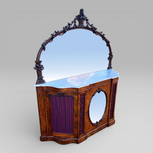 fig 1. A Victorian walnut credenza featuring a breakfront white marble top, an arched crest-carved mirror frame, and base panels detailed with an oval mirror and fabric behind fretwork.