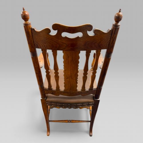 fig 4. A Victorian carved golden oak armchair featuring a pierced vertical slat backrest, sculpted armrests, turned legs, and a brown leather seat.