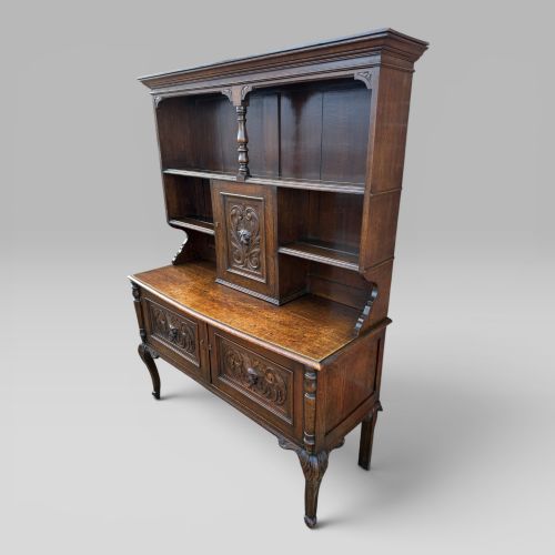 fig 1. A late Victorian dark oak dresser with carved Green Man foliate motifs on the cupboard doors, open display shelving, and cabriole legs.