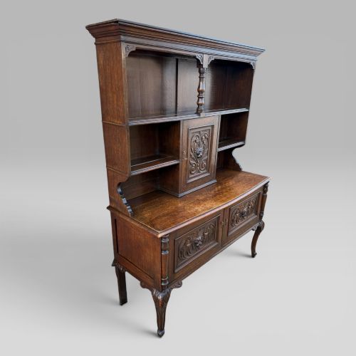 fig 2. A late Victorian dark oak dresser with carved Green Man foliate motifs on the cupboard doors, open display shelving, and cabriole legs.